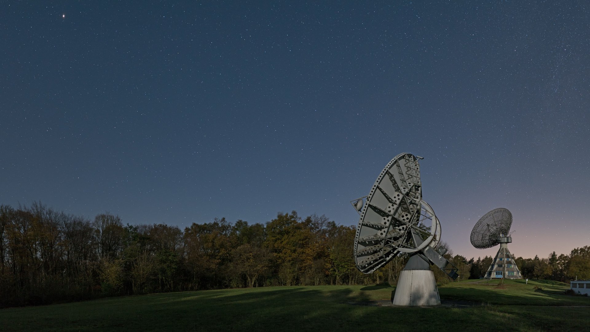Sternenpark Eifel erleben – Urlaub unter dem Sternenhimmel Radarschüsseln unter einem sternenklaren Nachthimmel auf einer Wiese bei Wald