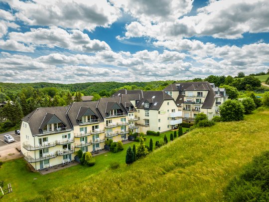 So erreichen Sie unsere Ferienwohnungen in Gemünd. Ferienpark mit modernen Wohngebäuden und grüner Landschaft unter bewölktem Himmel