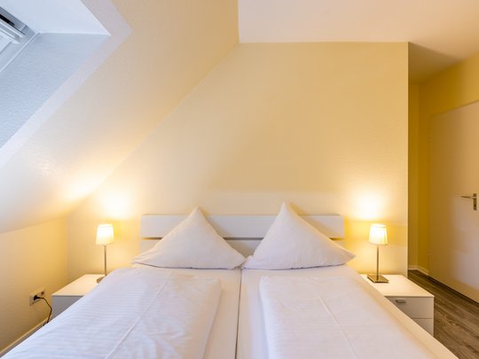 Ihre Unterkunft in Gemünd – Langzeitaufenthalt mit extra Service Gemütliches Schlafzimmer mit Doppelbett, weißen Kissen und zwei Nachttischlampen