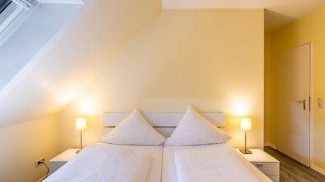Ferien in der Eifel: ein erster Einblick Gemütliches Schlafzimmer mit Doppelbett, weißen Kissen und zwei Nachttischlampen