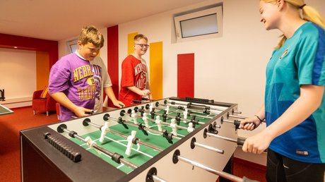 Ferien in der Eifel: ein erster Einblick Drei Jugendliche spielen Tischfußball in einem bunt gestalteten Raum