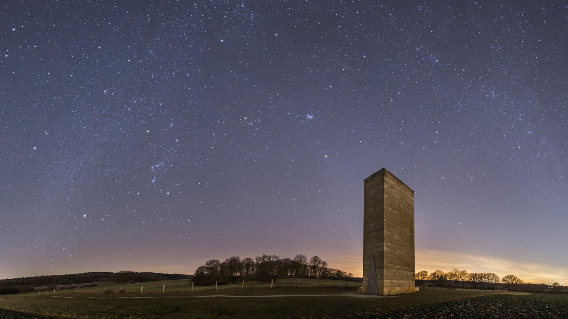 Sternenpark Eifel erleben – Urlaub unter dem Sternenhimmel Sternenhimmel über einer Landschaft mit einem hohen, rechteckigen Turm