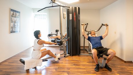 Ferien in der Eifel: ein erster Einblick Zwei Personen trainieren an Fitnessgeräten in einem hellen Raum mit Holzboden