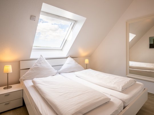 Ihre Unterkunft in Gemünd – Langzeitaufenthalt mit extra Service Helles Schlafzimmer mit Dachfenster, Doppelbett und Nachttischen mit Lampen