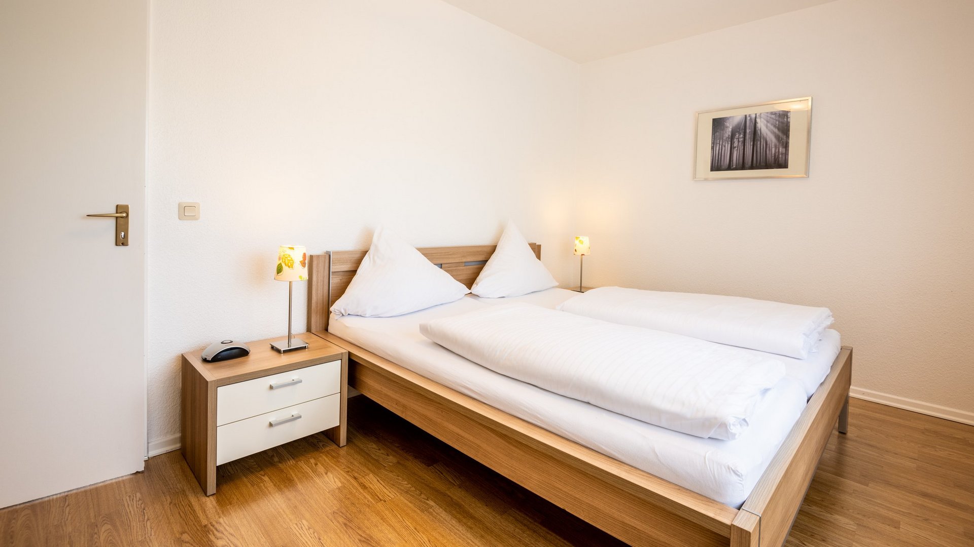 Ihre Unterkunft in Gemünd – Langzeitaufenthalt mit extra Service Helles Schlafzimmer mit Doppelbett, Nachttisch und Lampen