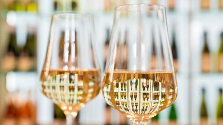 Ferien in der Eifel: ein erster Einblick Zwei Weingläser mit Roséwein vor einem Regal voller Weinflaschen