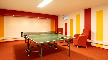 Ferien in der Eifel: ein erster Einblick Tischtennisplatte in einem Raum mit roten Sesseln und gestreifter Wand