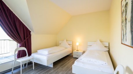 Ferien in der Eifel: ein erster Einblick Hell eingerichtetes Schlafzimmer mit zwei Einzelbetten und Nachttischlampe