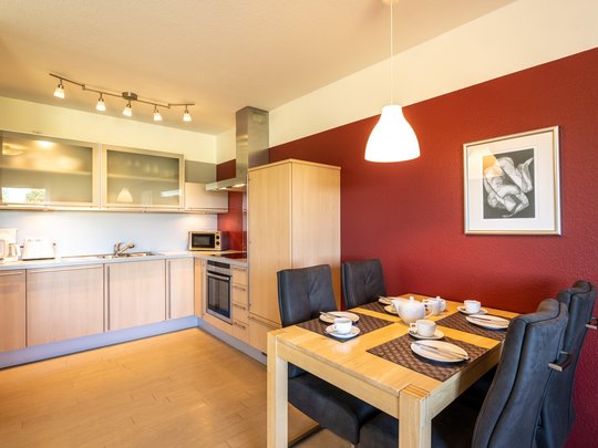 Ihre Unterkunft in Gemünd – Langzeitaufenthalt mit extra Service Moderne Küche mit Holzmöbeln, roter Wand und gedecktem Esstisch
