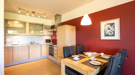 Ferien in der Eifel: ein erster Einblick Moderne Küche mit Holzmöbeln, roter Wand und gedecktem Esstisch