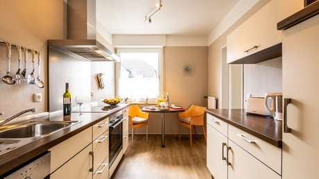 Ferien in der Eifel: ein erster Einblick Moderne Küche mit Esstisch, zwei orangenen Stühlen, Weinflasche und Küchengeräten