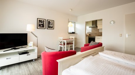 Ferien in der Eifel: ein erster Einblick Helle Einzimmerwohnung mit Bett, roten Sesseln, Fernseher, Esstisch und kleiner Küche