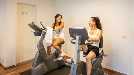 Ferien in der Eifel: ein erster Einblick Zwei Frauen unterhalten sich beim Training auf stationären Fahrrädern in einem Raum
