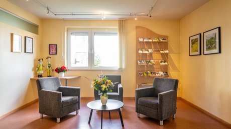 Ferien in der Eifel: ein erster Einblick Gemütlicher Wartebereich mit drei grauen Sesseln, Tisch und Blumenstrauß