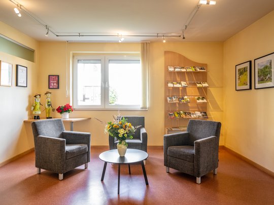 Wohnung mieten in Gemünd? Da haben wir was für Sie! Gemütlicher Wartebereich mit drei grauen Sesseln, Tisch und Blumenstrauß