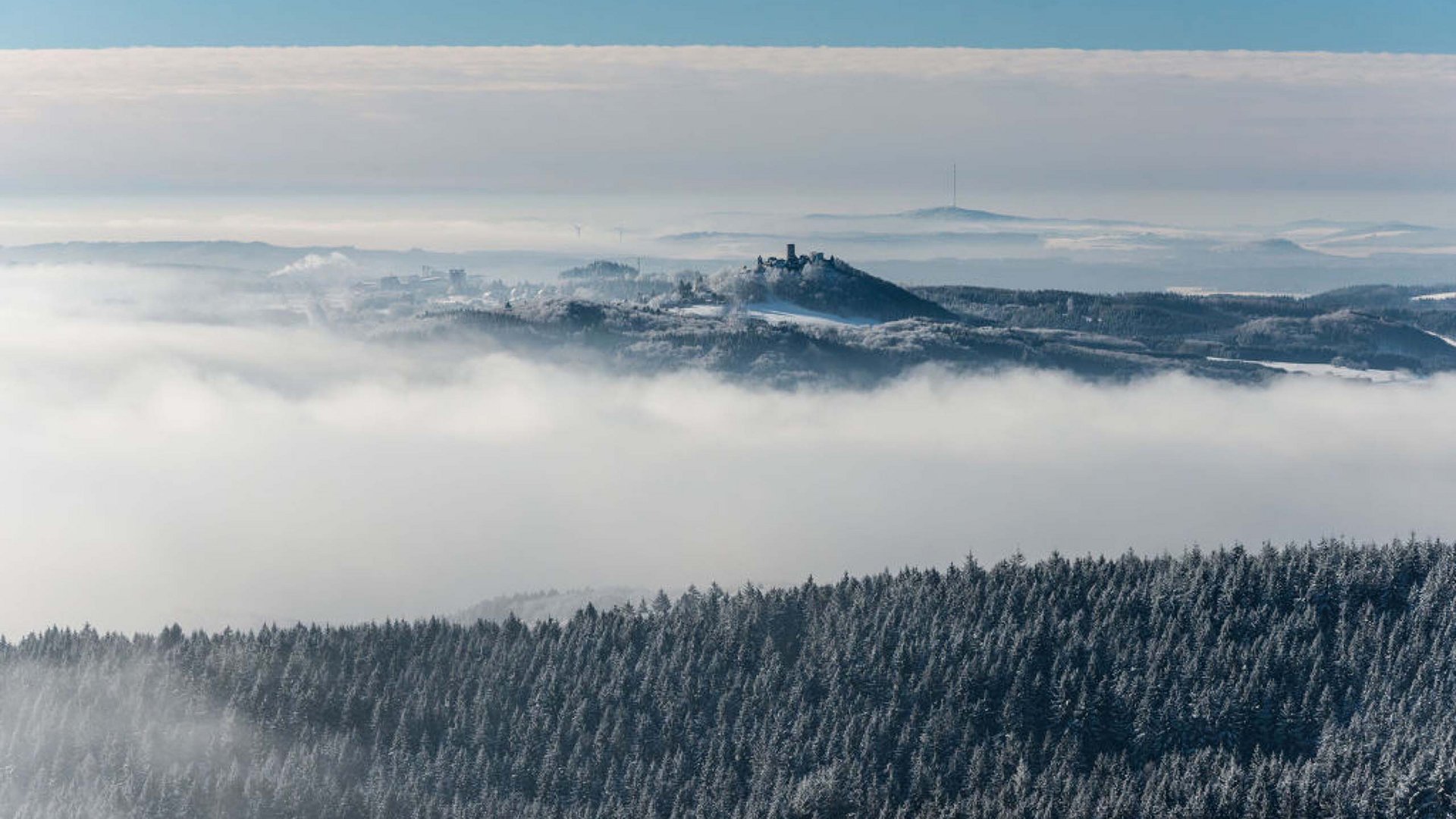 Erlebe die Eifel mit dem Fahrrad – Natur, Freiheit & Komfort Schneebedeckte Wälder und Nebel umgeben eine Burg auf einem Hügel