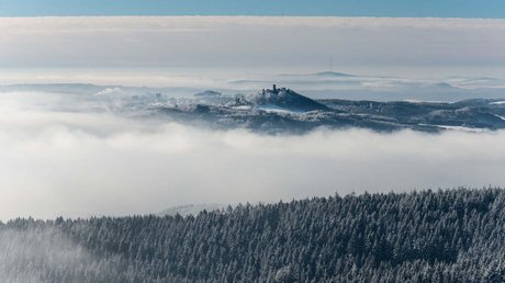 Ferien in der Eifel: ein erster Einblick Schneebedeckte Wälder und Nebel umgeben eine Burg auf einem Hügel