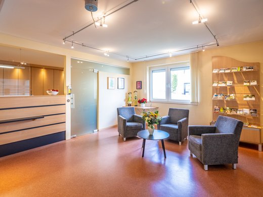 Wohnung mieten in Gemünd? Da haben wir was für Sie! Wartebereich mit drei Sesseln, Blumen auf Tisch, Empfangstresen und Infomaterial