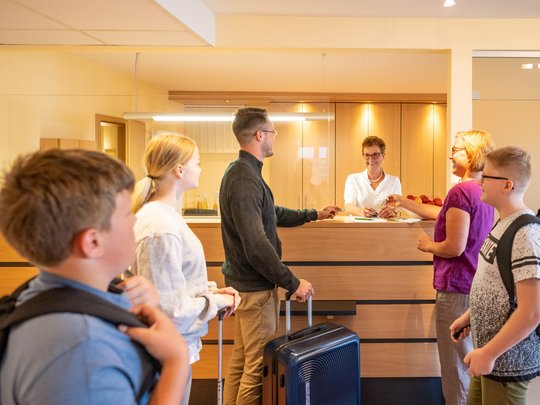 So erreichen Sie unsere Ferienwohnungen in Gemünd. Familie checkt an der Hotelrezeption mit Kinder und Koffern ein
