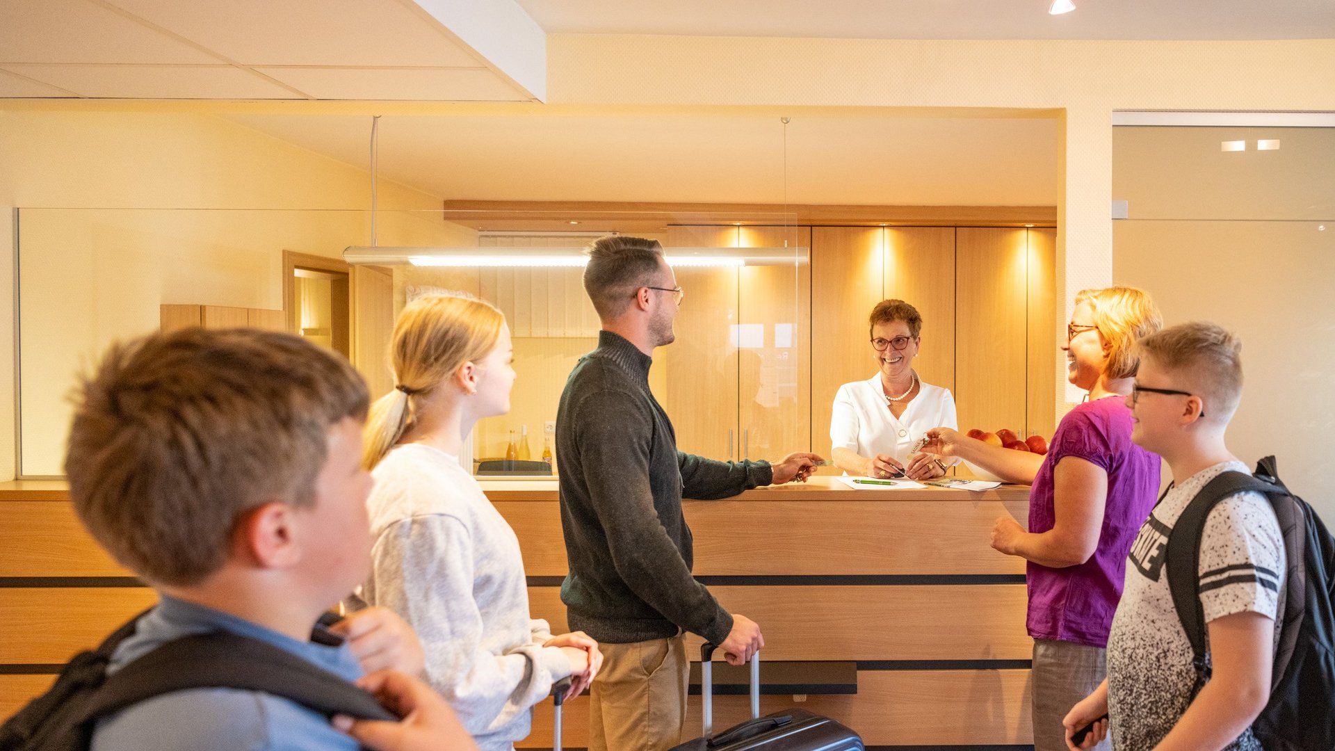 Gemünder Ferienpark: Jobs, die erfüllen Familie checkt an der Hotelrezeption mit Kinder und Koffern ein