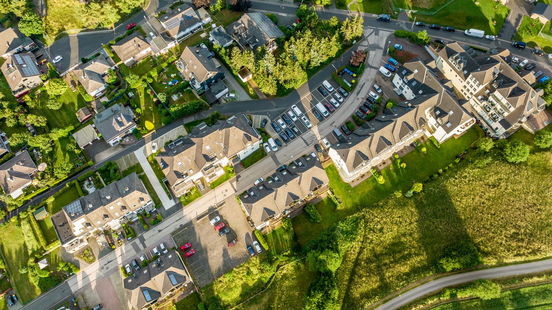 So erreichen Sie unsere Ferienwohnungen in Gemünd. Luftaufnahme eines Wohngebiets mit Häusern, Autos und grünen Wiesen
