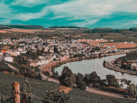 Urlaub in Deutschland: Von der Eifel aus Städte erkunden Blick auf eine Stadt an einem Fluss mit Weinbergen und Hügeln im Hintergrund