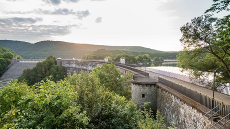 Ferien in der Eifel: ein erster Einblick Stauseemauer mit Bäumen im Vordergrund und Hügeln im Hintergrund bei Sonnenuntergang