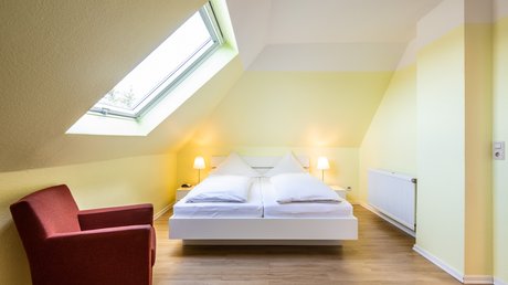 Ferien in der Eifel: ein erster Einblick Helles Schlafzimmer mit Dachfenster, Doppelbett und rotem Sessel