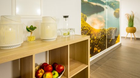 Ferien in der Eifel: ein erster Einblick Holzregal mit Äpfeln, Lampen und Gläsern vor Wand mit Naturbild