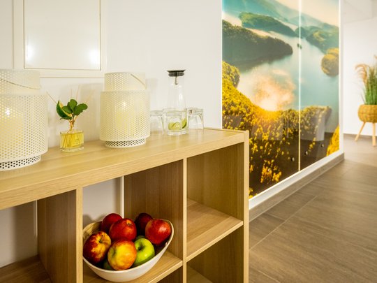 Wohnung mieten in Gemünd? Da haben wir was für Sie! Holzregal mit Äpfeln, Lampen und Gläsern vor Wand mit Naturbild