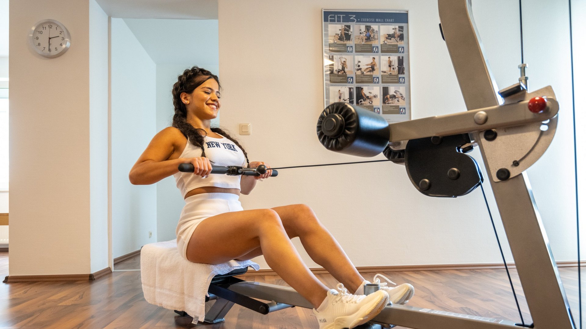 Eine Ferienwohnung in der Eifel mit Sauna und Gym Frau trainiert am Rudergerät in hellem Fitnessraum mit Übungsplakat an Wand