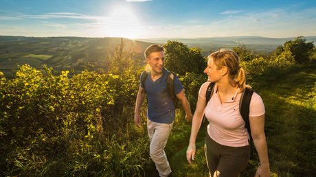 Ferien in der Eifel: ein erster Einblick Paar wandert bei Sonnenuntergang durch grüne Hügel