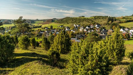 Ferien in der Eifel: ein erster Einblick Landschaft mit grünen Hügeln und einem Dorf mit weißen Häusern unter blauem Himmel