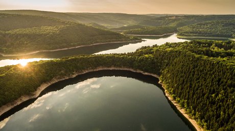 Ferien in der Eifel: ein erster Einblick Luftaufnahme von bewaldeten Hügeln und einem See bei Sonnenuntergang