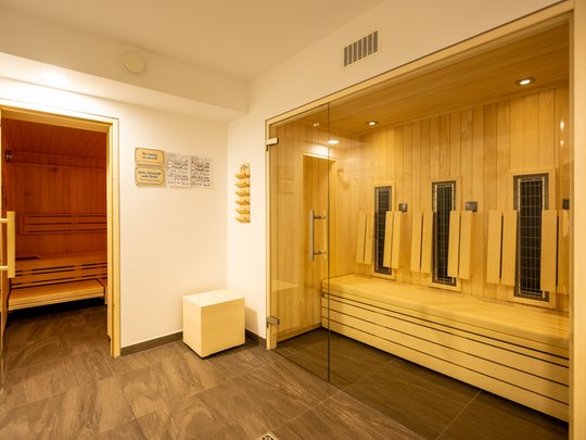 Alle aktuellen Angebote, Specials und Raten im Gemünder Ferienpark Salzberg – perfekt für euren Urlaub im Nationalpark Eifel. Innenansicht eines modernen Saunabereichs mit Holzverkleidung und Glaswand