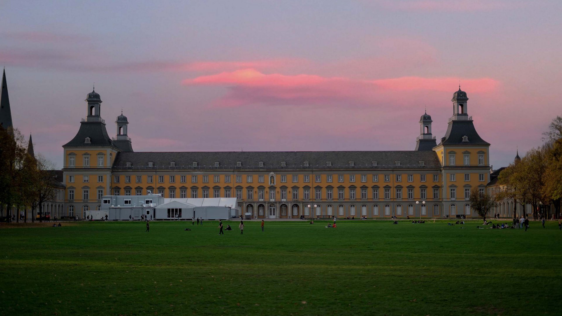 Urlaub in Deutschland: Von der Eifel aus Städte erkunden Schloss bei Sonnenuntergang mit pinkfarbenem Himmel und Menschen auf der Wiese