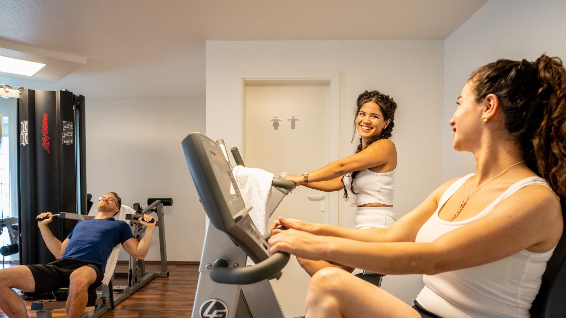 Wohnung mieten in Gemünd? Da haben wir was für Sie! Drei Personen trainieren in einem Fitnessstudio an verschiedenen Geräten.