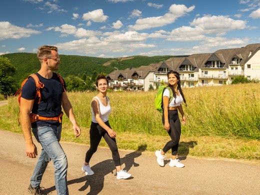 Ferienwohnungen in Gemünd mit dem gewissen Extra Drei junge Leute wandern auf sonnigem Landweg mit Ferienpark im Hintergrund