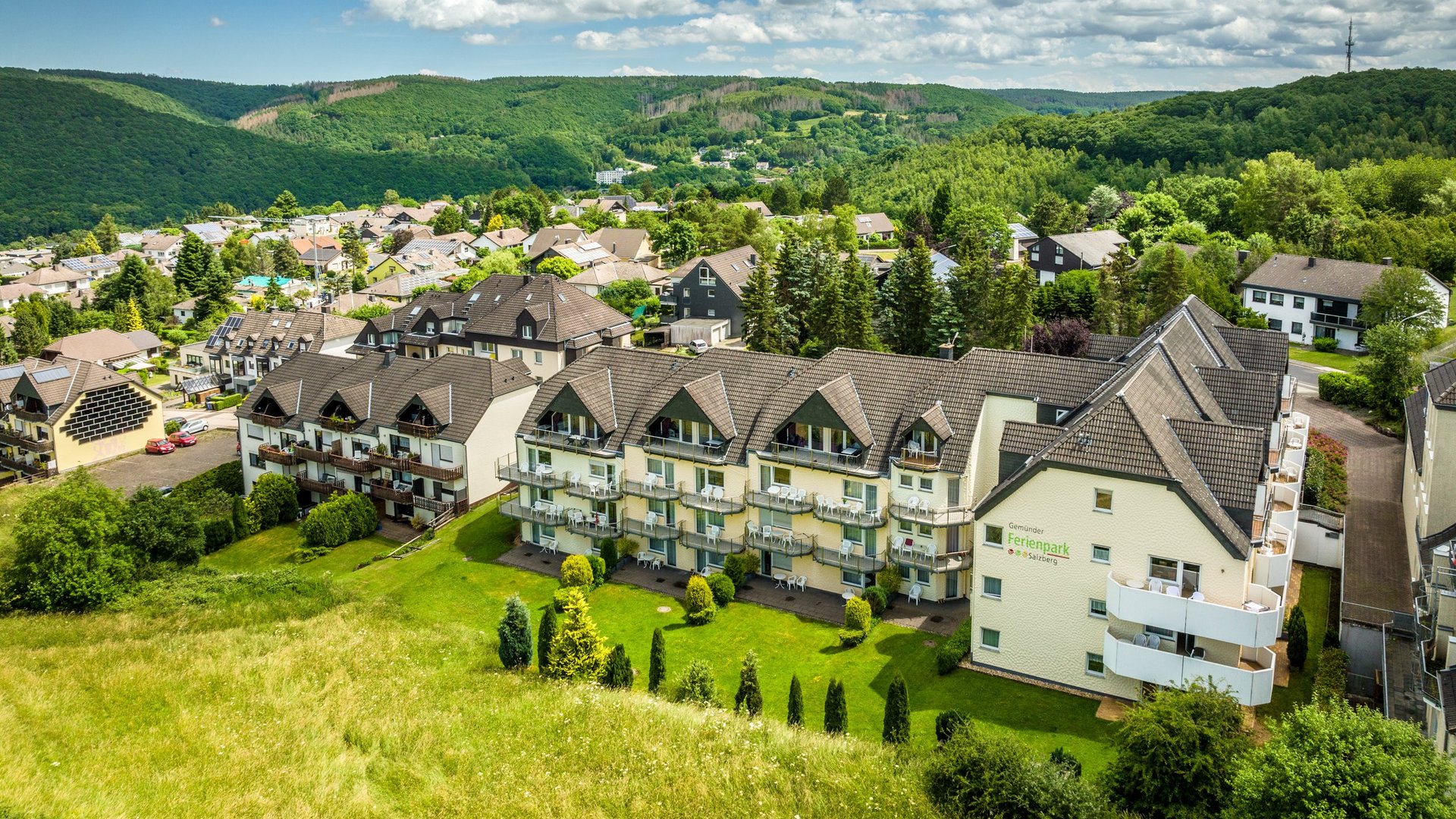 Ferienwohnungen in Gemünd mit dem gewissen Extra Blick auf Ferienpark mit Häusern und grünen Hügeln unter blauem Himmel