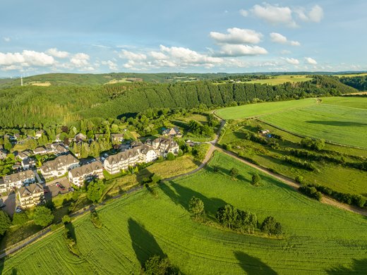 Holidays in the Eifel region: Want a change of pace? Aerial view of a village with green fields and wooded hills in sunlight