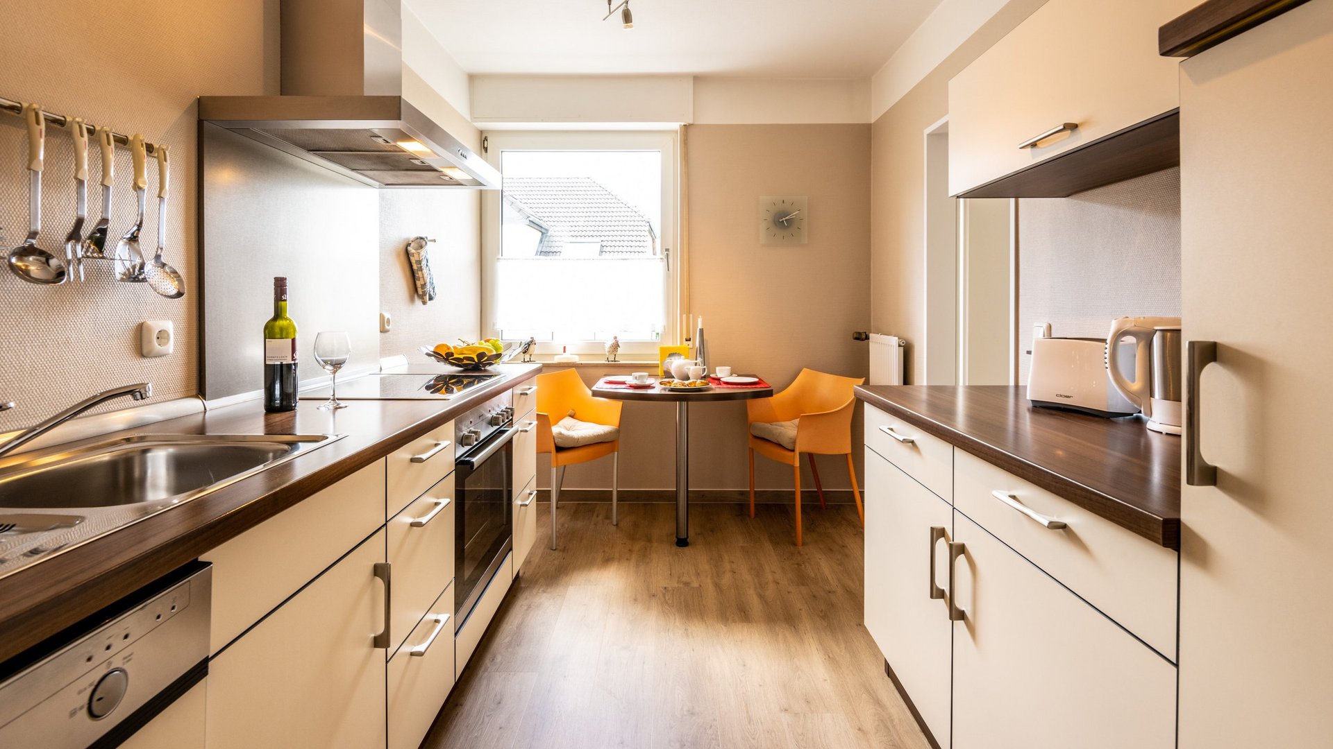 Ferienwohnungen in Gemünd mit dem gewissen Extra Moderne Küche mit Esstisch, zwei orangenen Stühlen, Weinflasche und Küchengeräten