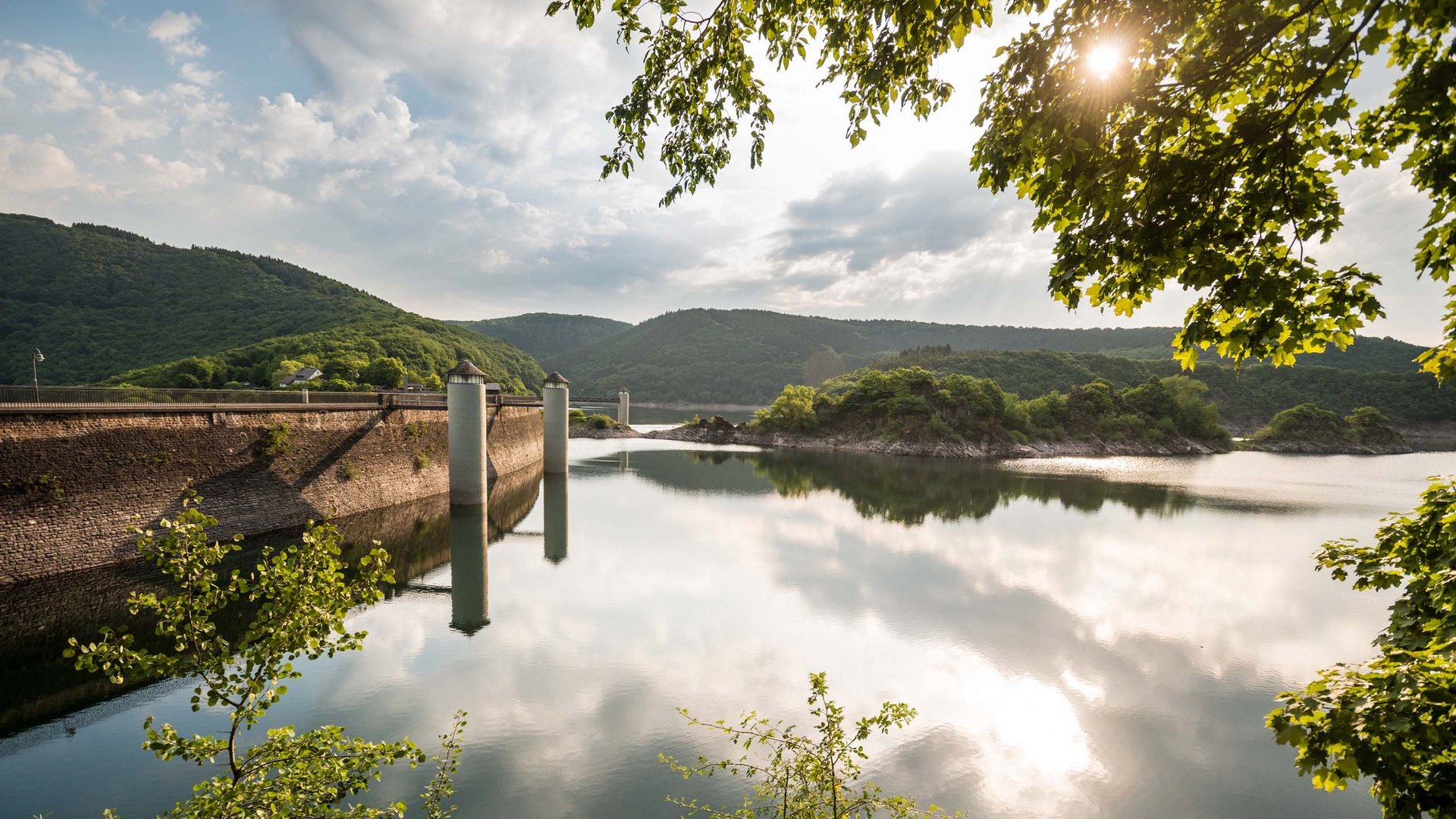 Holidays in the Eifel region: Want a change of pace? Dam with water and forested hills under cloudy sky