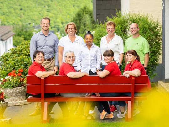 Ferienwohnungen in Gemünd mit dem gewissen Extra Gruppe von neun lächelnden Personen, einige auf einer roten Bank sitzend, draußen im Grünen