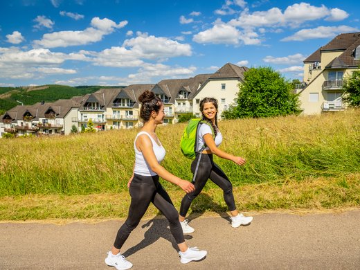 Holidays in the Eifel region: Want a change of pace? Two women hiking on a path with houses and fields in the background.