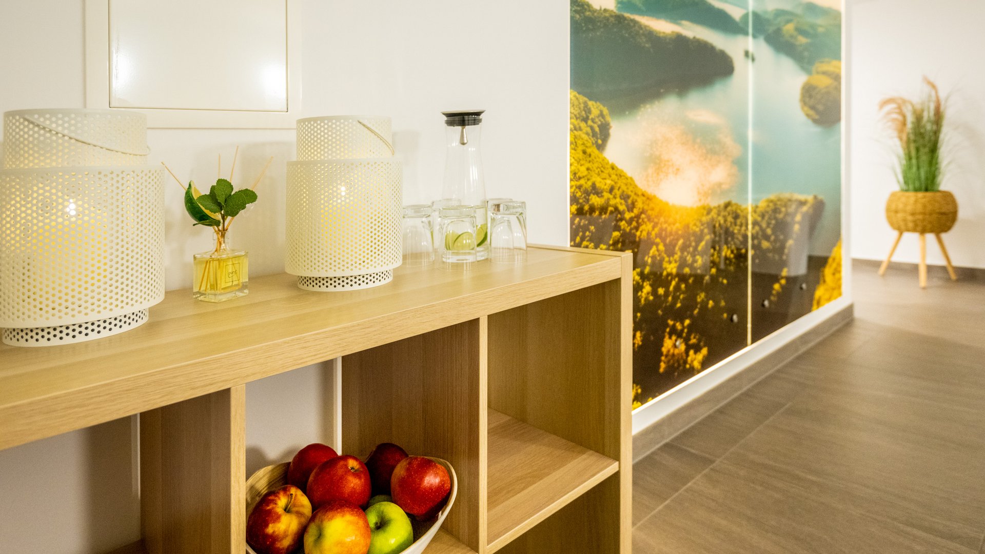 Ferienwohnungen in Gemünd mit dem gewissen Extra Holzregal mit Äpfeln, Lampen und Gläsern vor Wand mit Naturbild